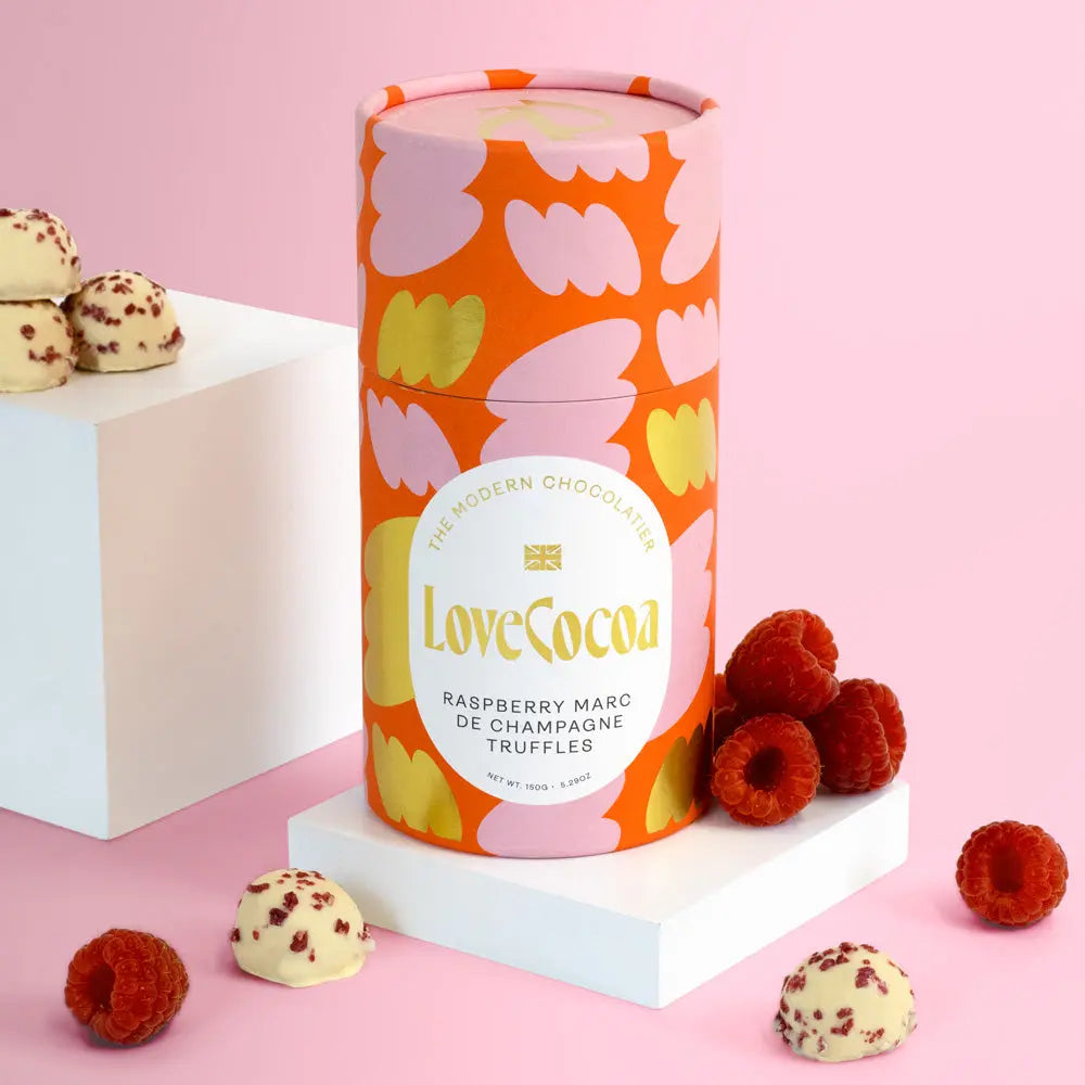 Decorative cylindrical container with modern design and 'LoveCocoa' branding, surrounded by truffles and raspberries on a pink background.