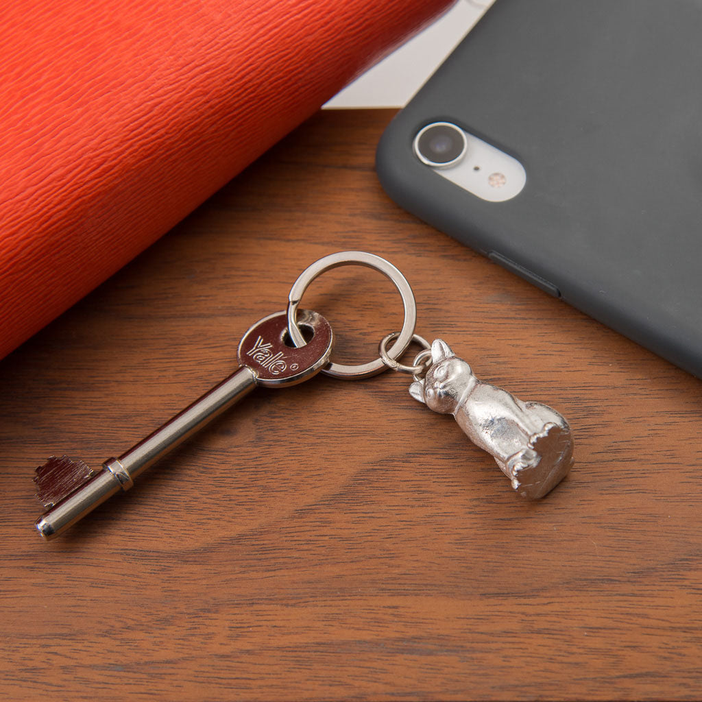 Keychain with a key and cat-shaped charm on a wooden surface next to a phone.