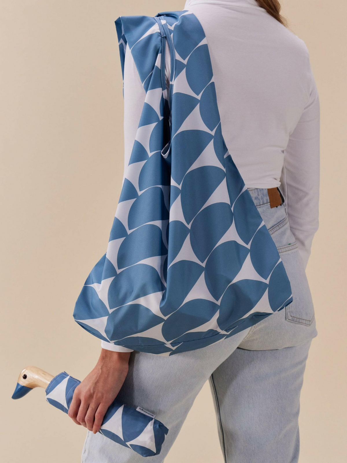 Person holding a blue and white patterned bag with a beige background