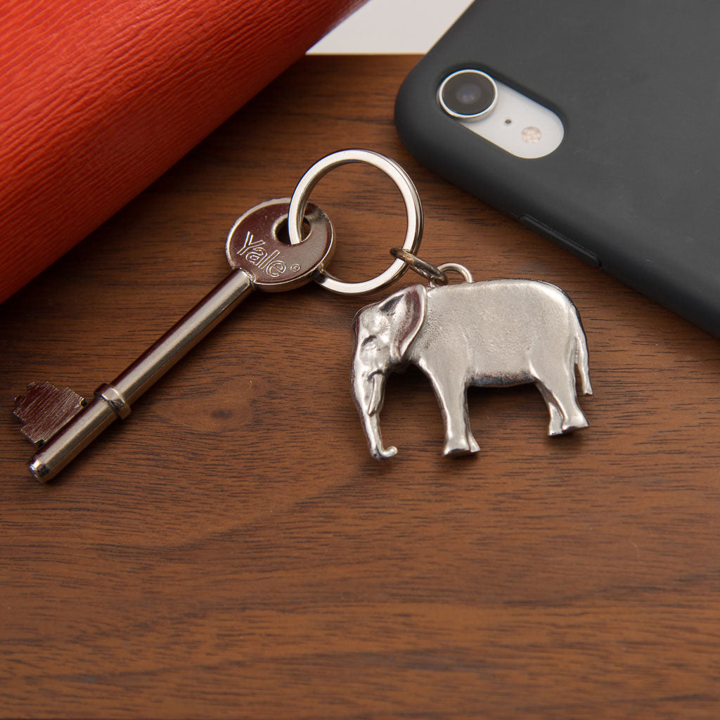 Keychain with elephant charm and key on a wooden surface next to a phone