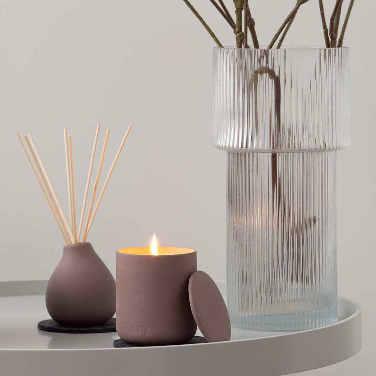 Decorative items including a candle, diffuser, and vase on a white surface with a light gray background.