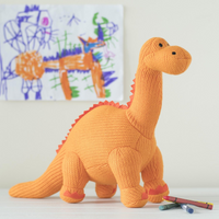 Knitted dinosaur toy in front of children's drawings on a white wall.