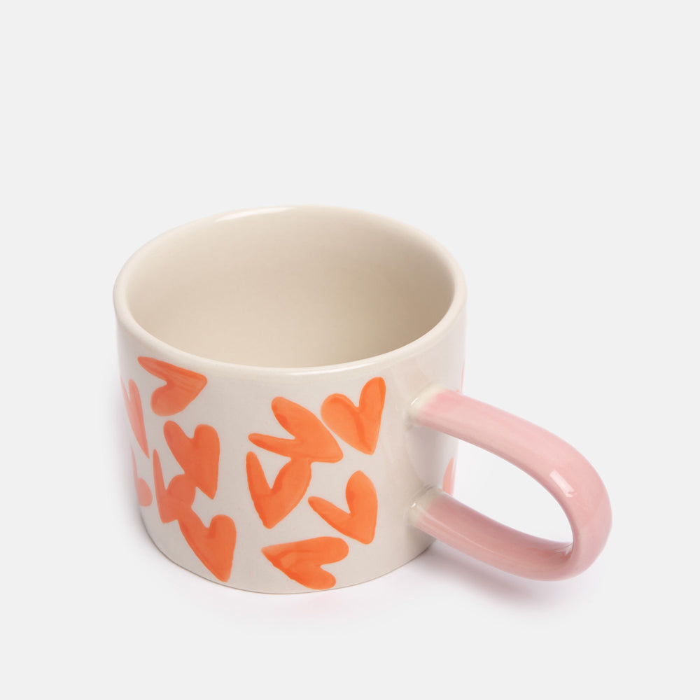 Mug with orange heart patterns and a pink handle on a white background