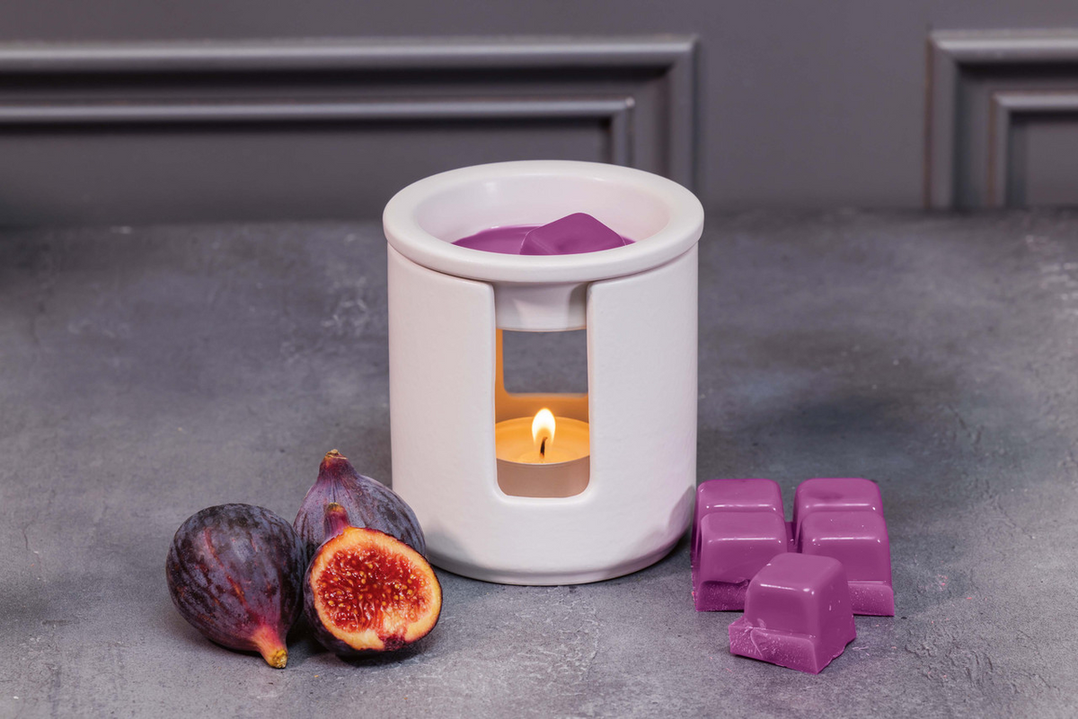 White wax warmer with a lit candle and purple wax cubes on a gray surface.